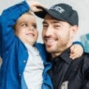A police officer and his son smiling together as his son plays with his hat.