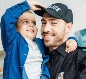 A police officer and his son smiling together as his son plays with his hat.