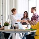 A office conference room full of coworkers congratulating a fellow coworker for an award.