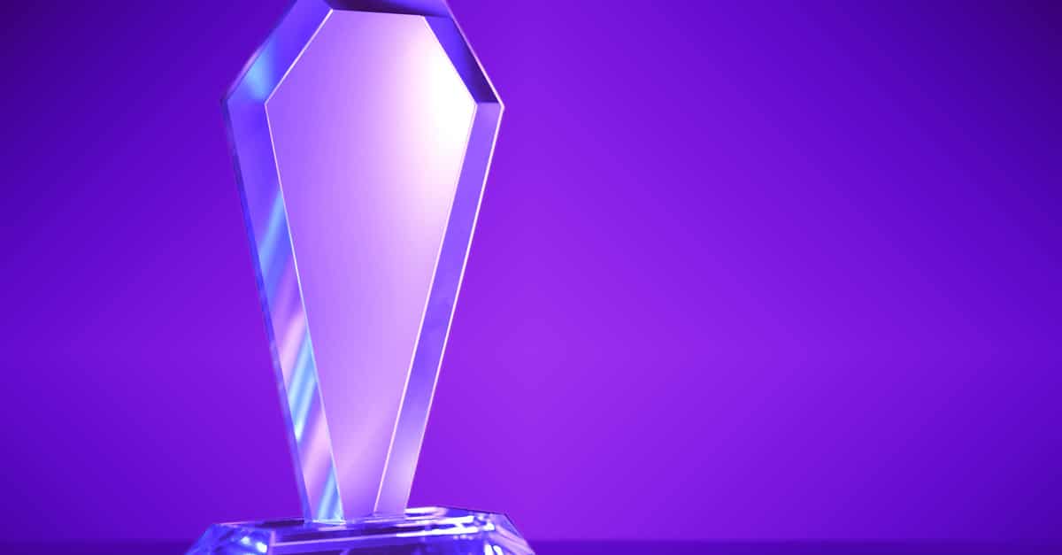 A blank crystal award sits on a solid surface against a purple gradient background. Light reflects off the award.