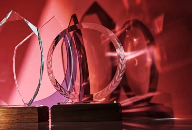 Four transparent awards of unique shapes with wood bases reflect shades of light and shadowing on a red background.