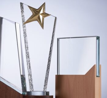 Three crystal plaques in different shapes and sizes are on a table. The middle plaque has a gold star on top.