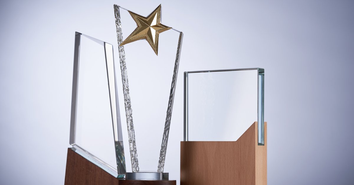 Three crystal plaques in different shapes and sizes are on a table. The middle plaque has a gold star on top.